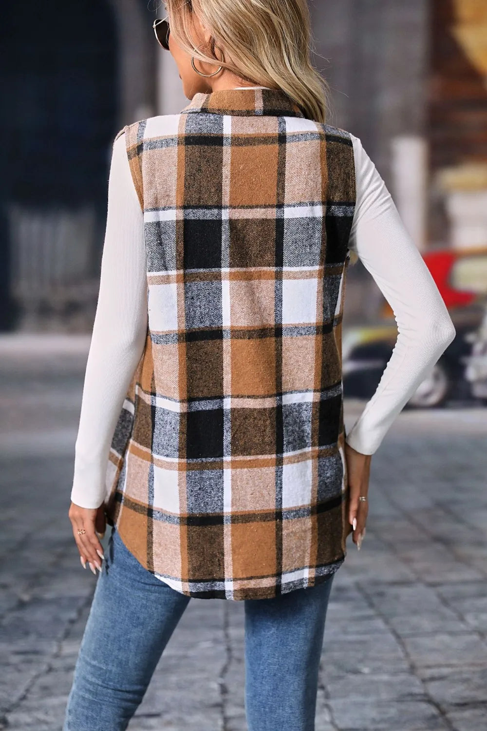 Woman wearing a camel plaid button-up vest coat layered over a white turtleneck with blue jeans and gold jewelry for a cozy fall outfit.