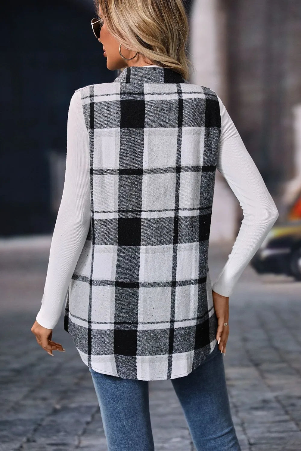 Woman wearing a gray plaid button-up vest coat layered over a white turtleneck with blue jeans and gold jewelry for a cozy fall outfit.