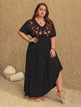 Woman wearing a black dress with floral embroidery against a beige wall.
