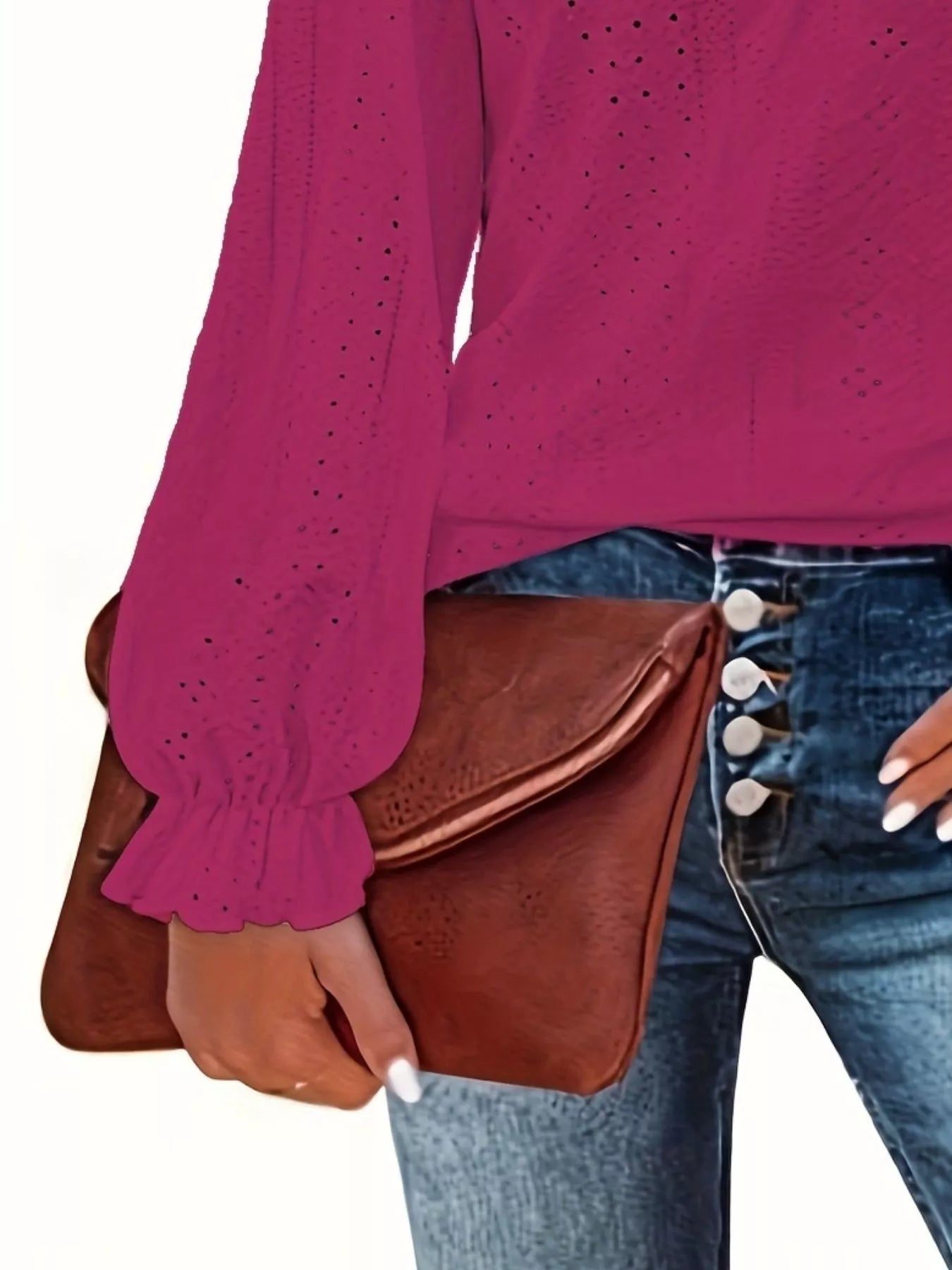 Person wearing a rose red blouse and blue jeans holding a brown leather clutch.