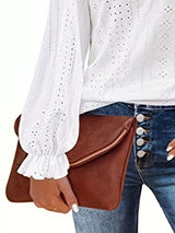 Person holding a brown leather clutch bag with a white blouse and blue jeans.
