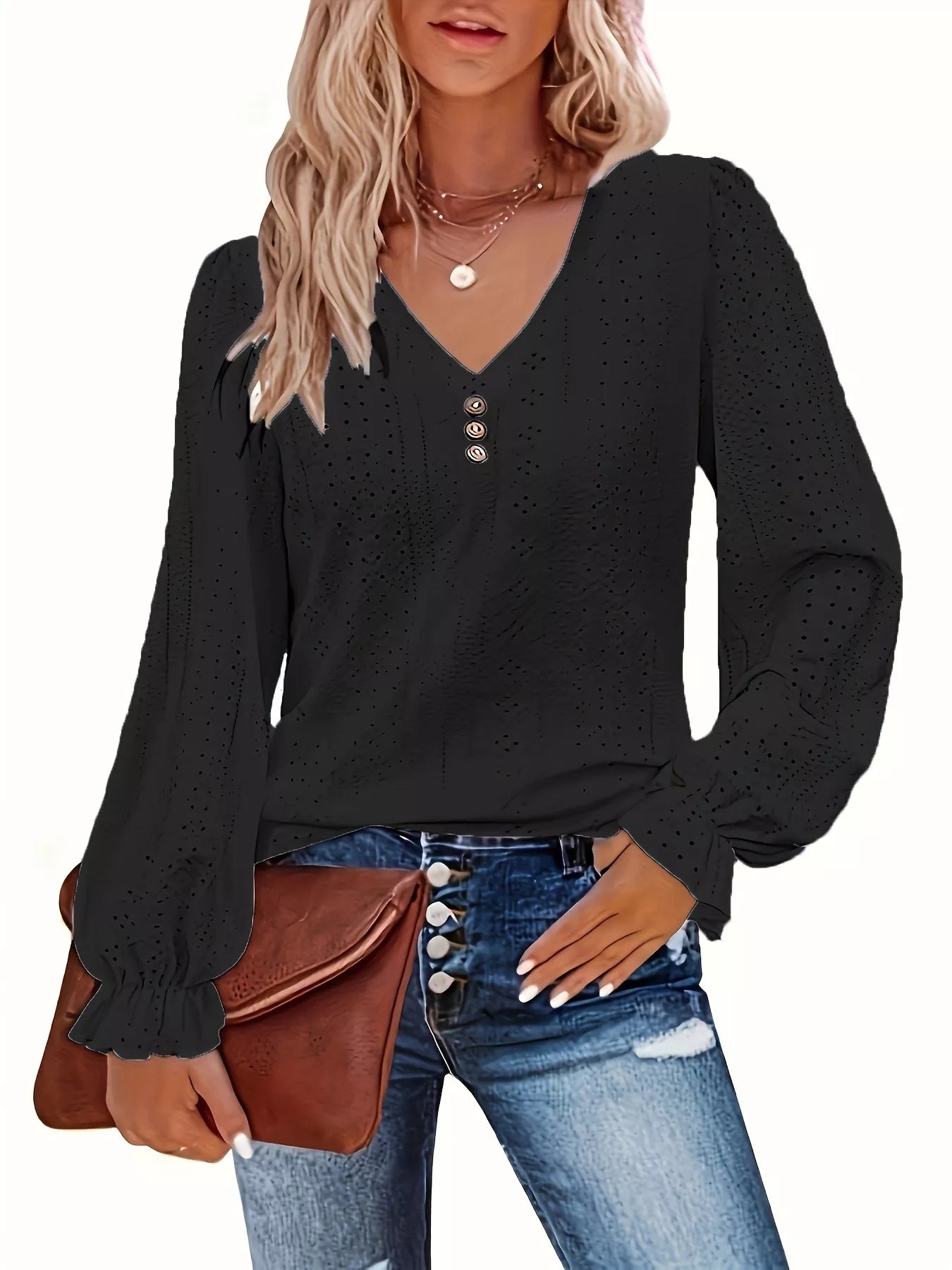Woman wearing a black long-sleeve top with eyelet details, blue jeans, and holding a brown leather bag.