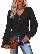 Woman wearing a black long-sleeve top with eyelet details, blue jeans, and holding a brown leather bag.