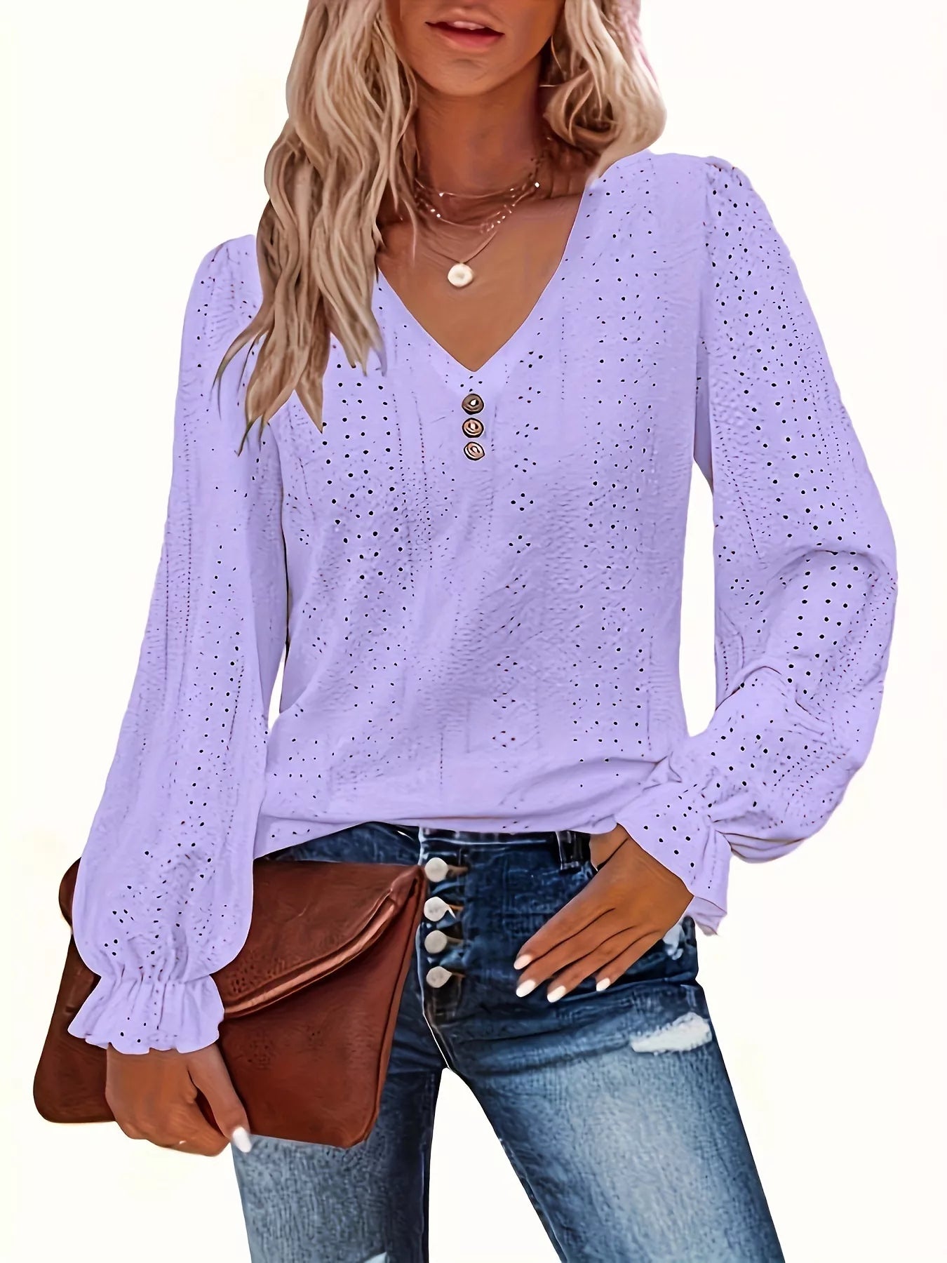 Woman wearing a light purple long-sleeve blouse with eyelet details, paired with jeans and a brown bag.