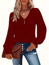 Woman wearing a red long-sleeve top with a V-neckline, holding a brown clutch against a white background.