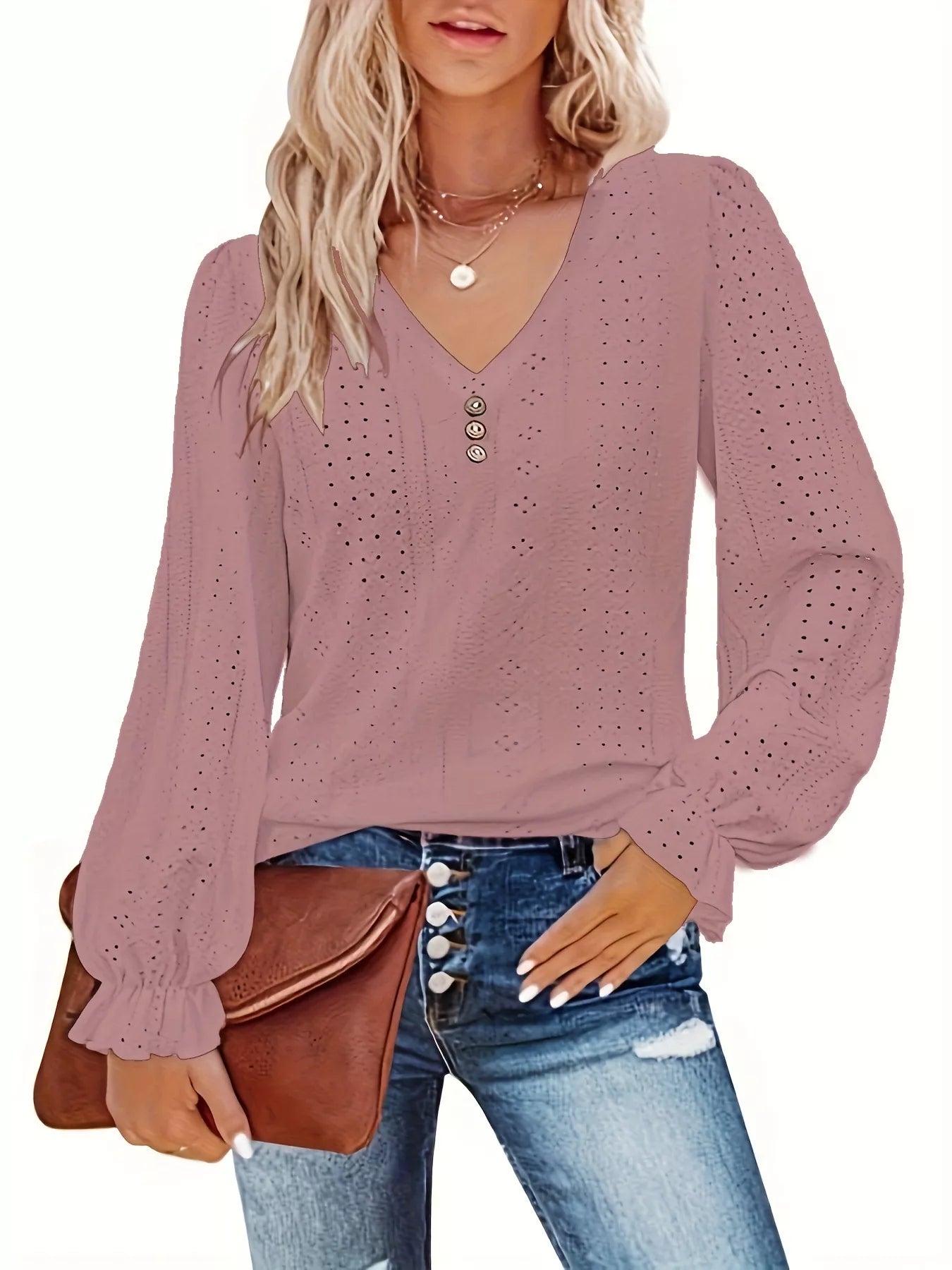Woman wearing a rouge color long-sleeve top with eyelet details, holding a brown clutch.