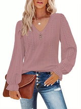 Woman wearing a rouge color long-sleeve top with eyelet details, holding a brown clutch.