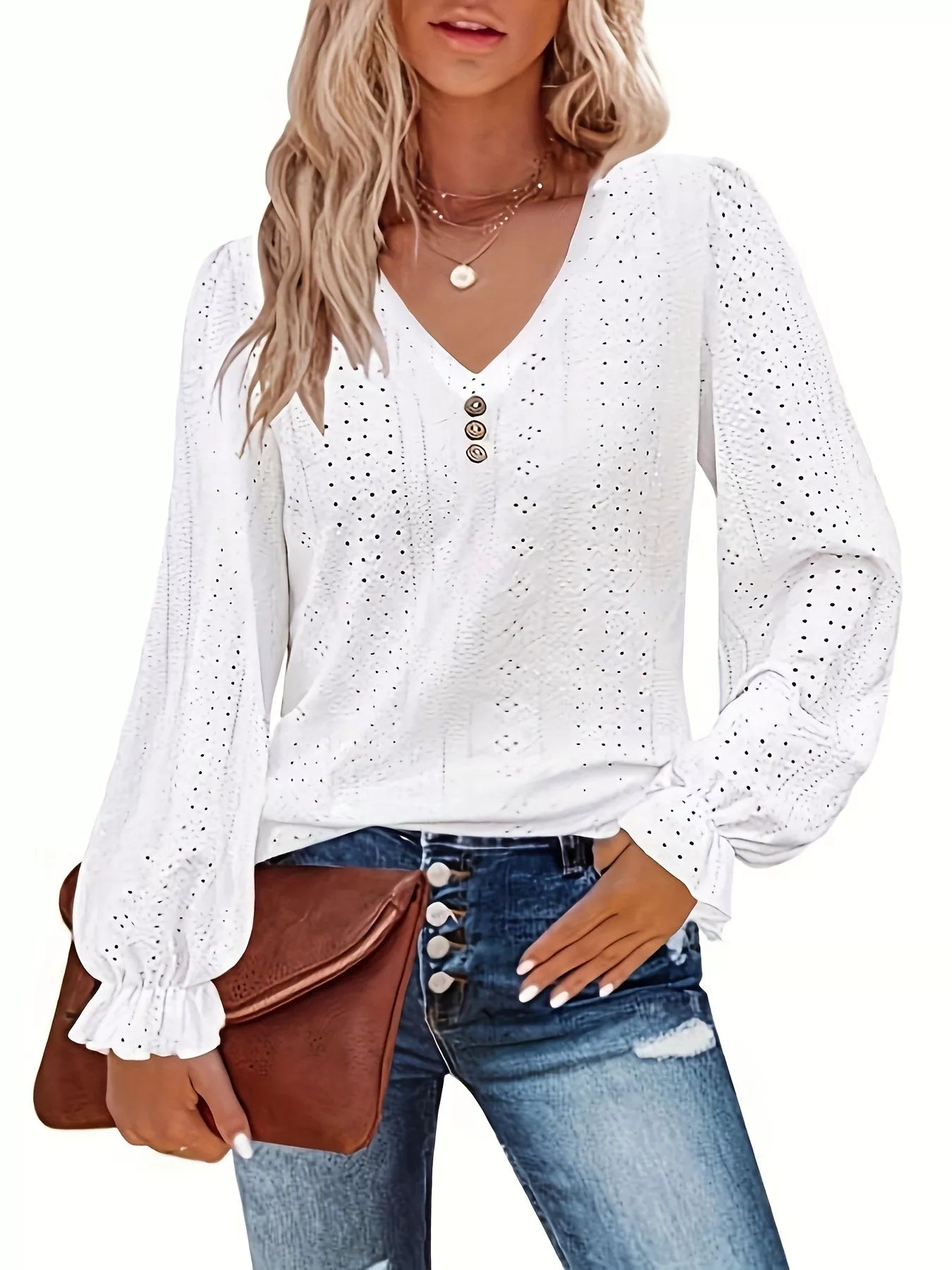 Woman wearing a white blouse with long sleeves and blue jeans, holding a brown clutch.