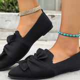 Black loafers with bow details worn by a person on a light background