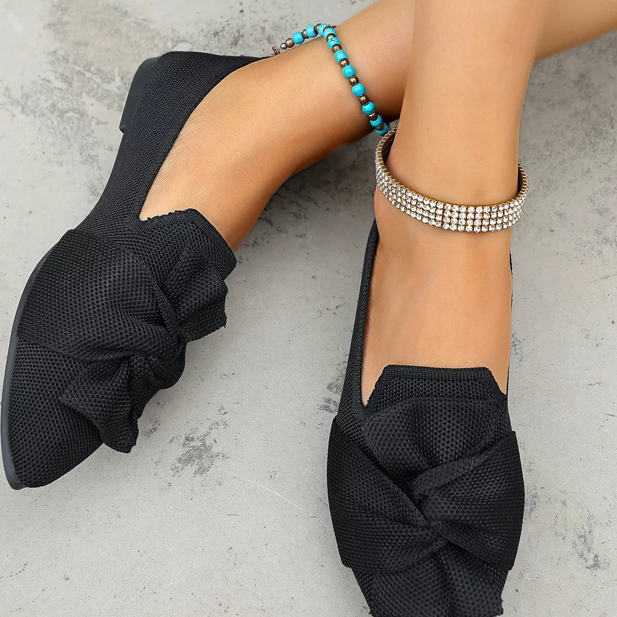 Black flat shoes with a bow detail worn by a person on a light gray surface.
