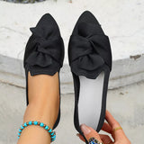 Black pointed-toe flats with large bows held by a person against a light background