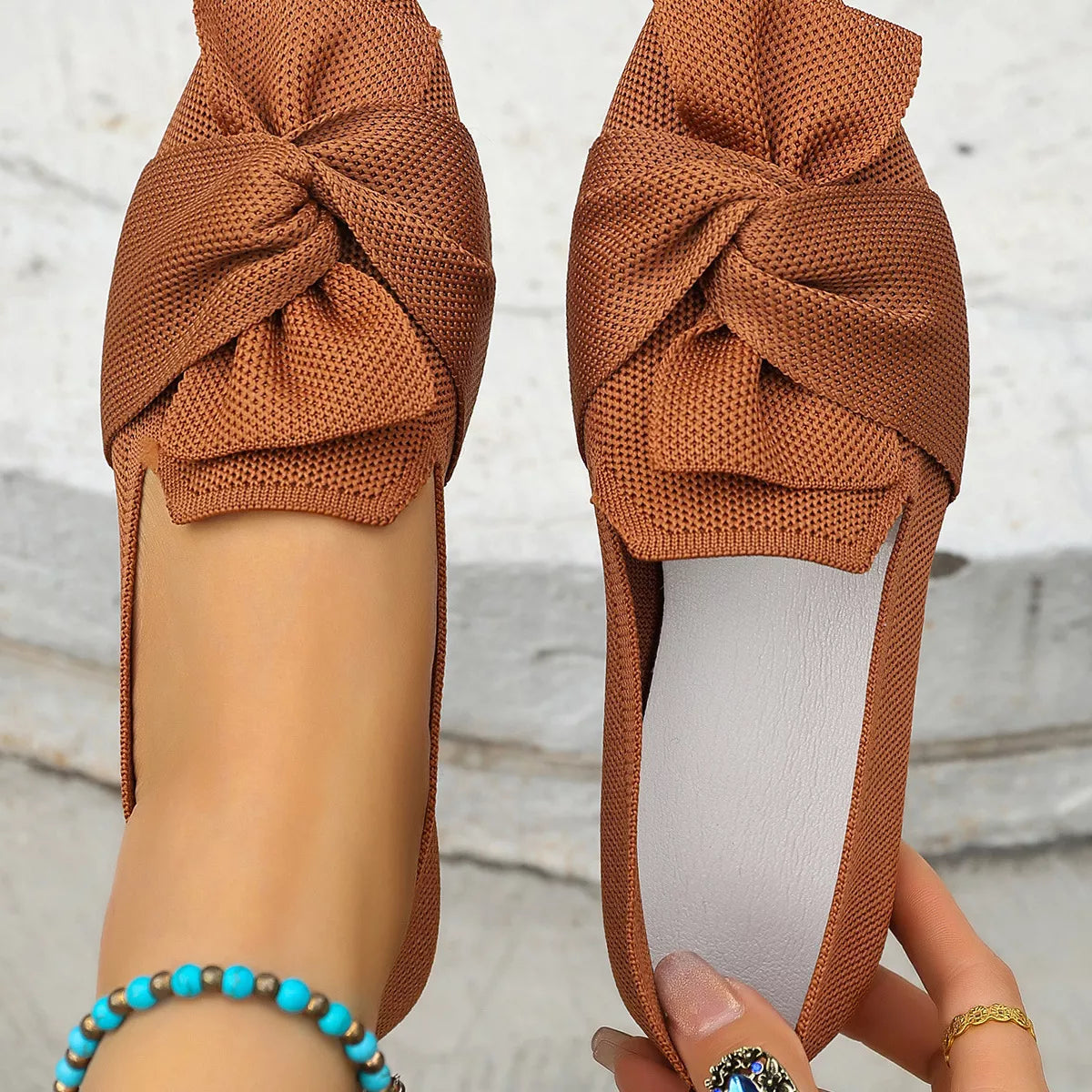 Brown shoes with knotted design held by a person against a light background