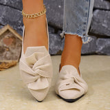 Beige pointed-toe shoes with a bow detail worn by a person, with a blurred background.