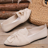 Pair of beige loafers with a bow detail on a wooden surface.