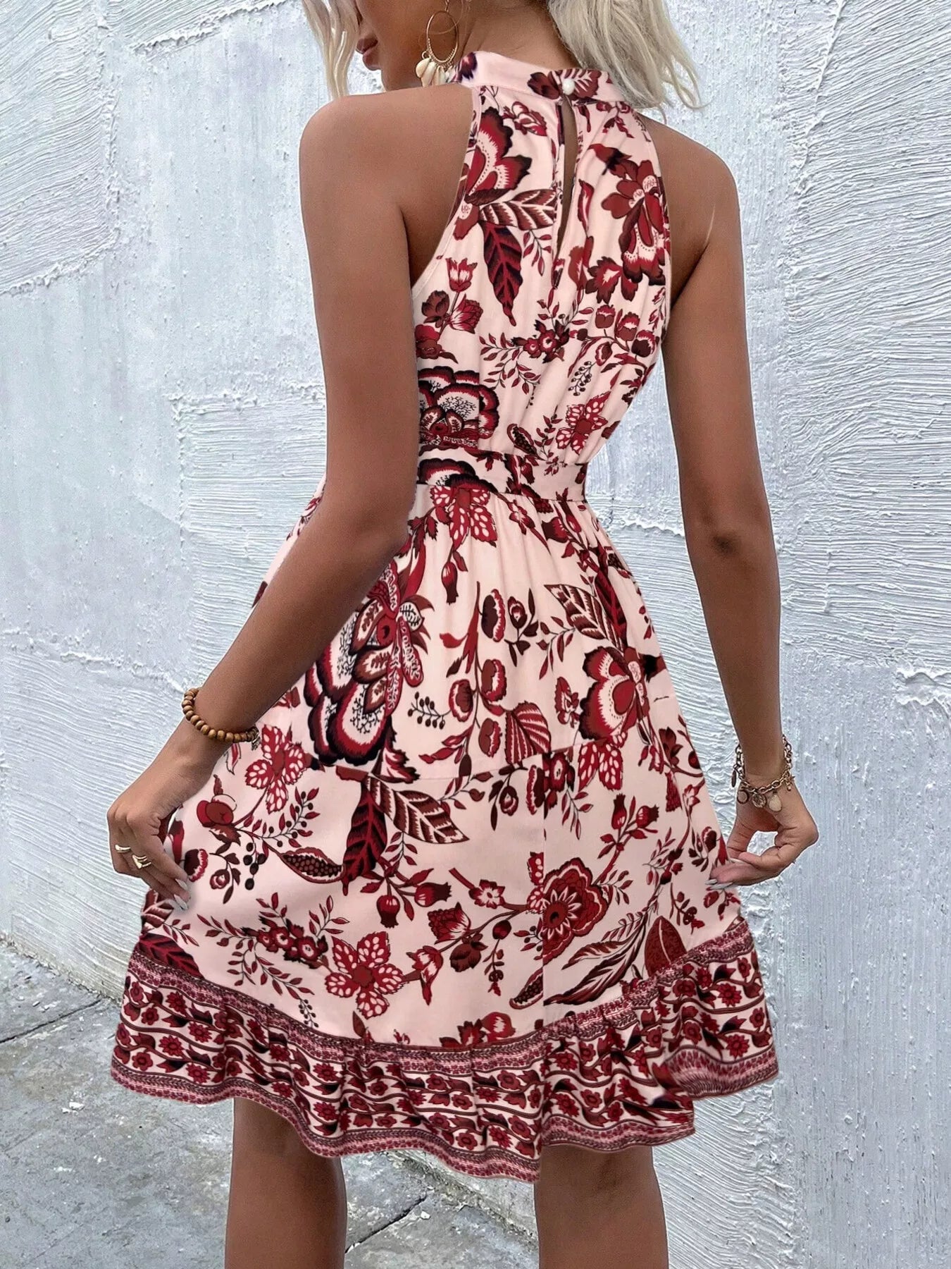 Woman wearing a floral dress against a textured wall. Showing Back