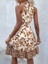 Woman wearing a tan floral dress against a light gray wall showing the back of dress.