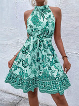Woman wearing a teal floral dress against a textured white wall.