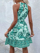 Teal floral dress worn by a person against a light gray wall showing the back of dress.