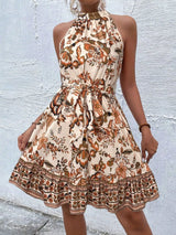 Woman wearing a tan floral dress against a textured white wall.