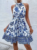 Woman wearing a blue and white floral dress against a textured white wall.