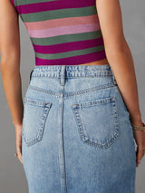 Woman wearing a light wash denim midi skirt with front slit, pockets and raw hem.