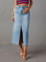 Woman wearing a light wash denim midi skirt with front slit, pockets and raw hem.