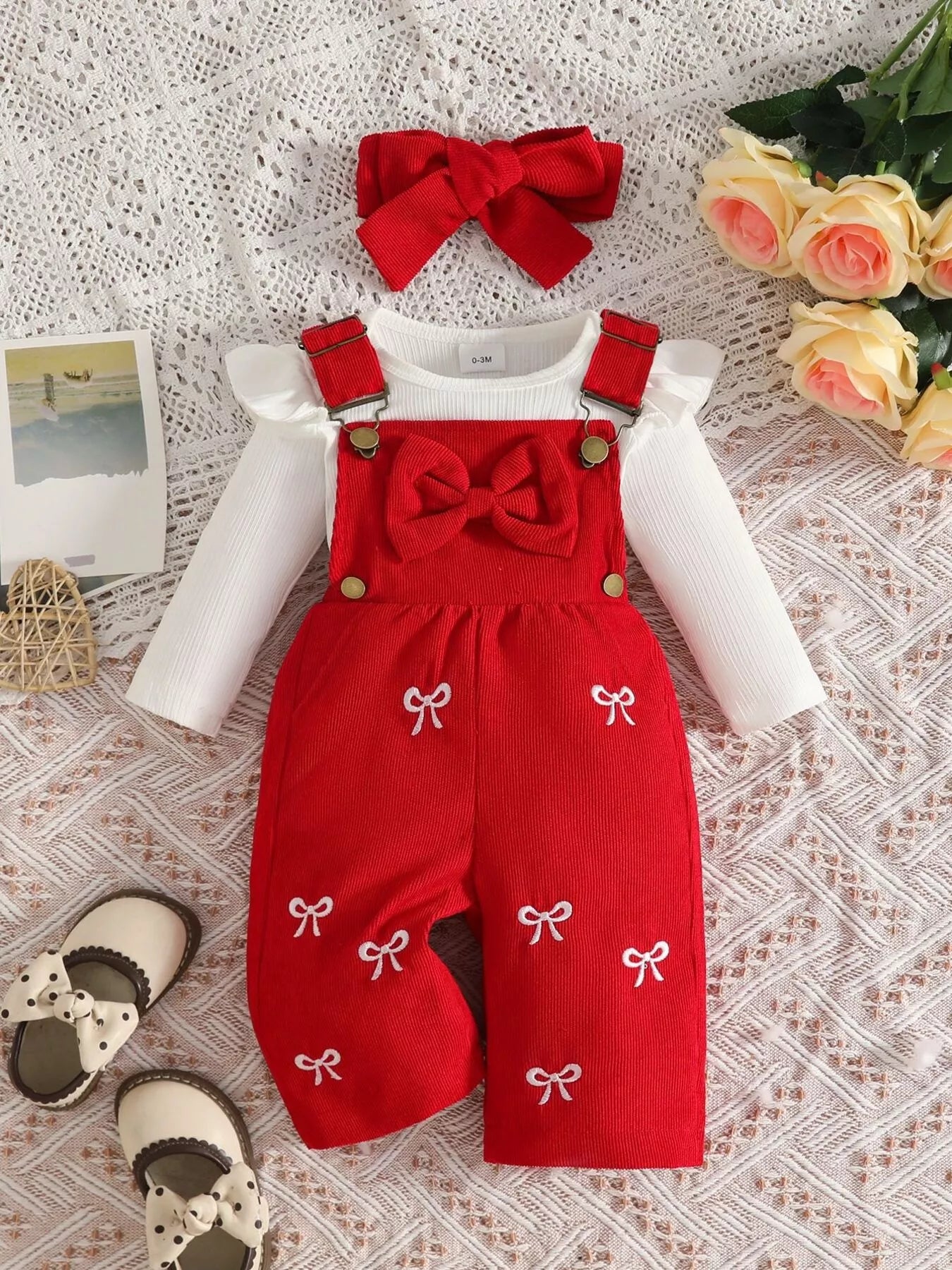 Baby girl three-piece outfit featuring a cream ribbed long-sleeve bodysuit with ruffled shoulders, red bow-embroidered overalls and matching red bow headband.
