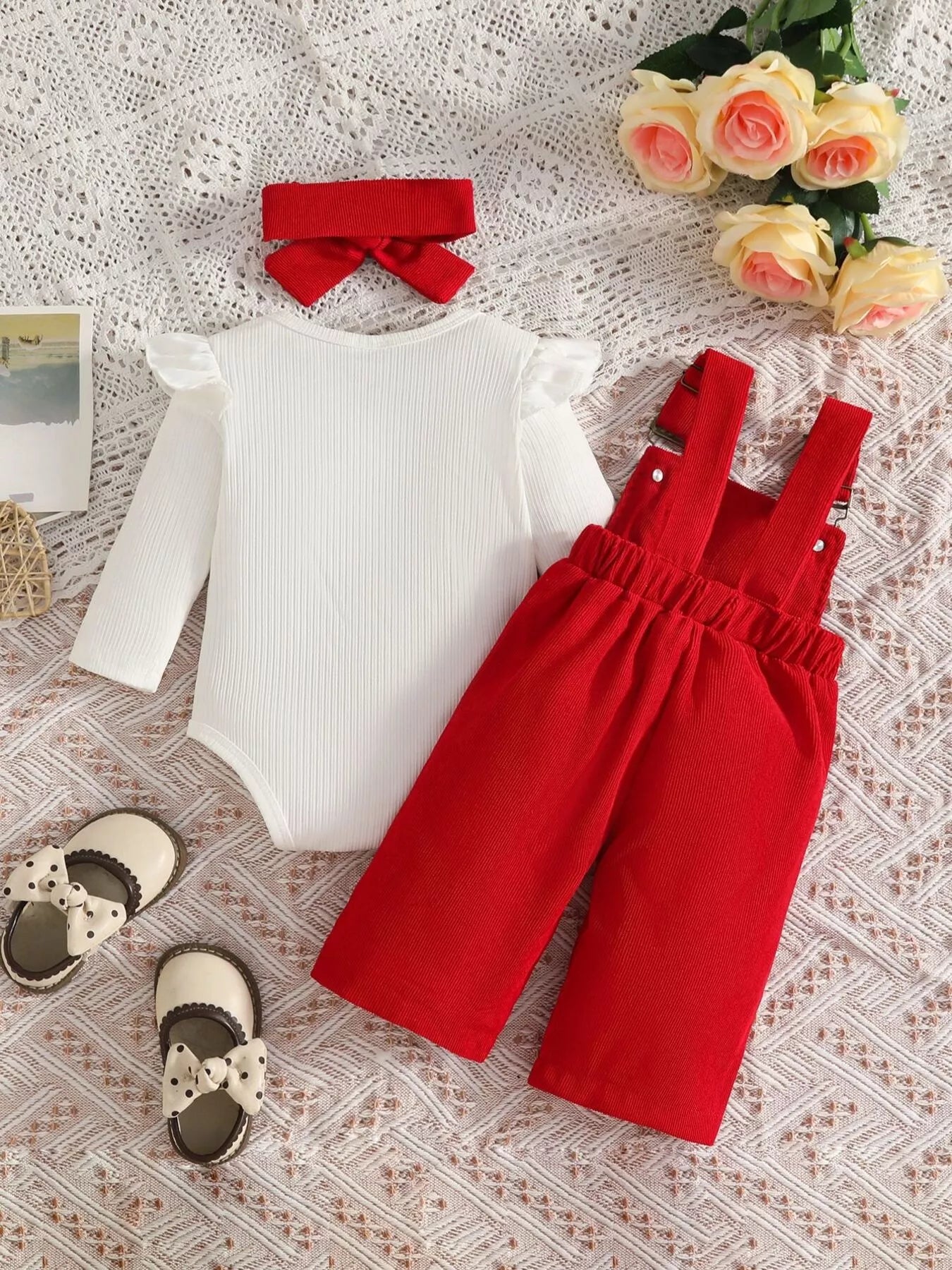 Baby girl three-piece outfit featuring a cream ribbed long-sleeve bodysuit with ruffled shoulders, red bow-embroidered overalls and matching red bow headband.