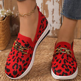 Red leopard print shoes with gold accents worn by a person on a textured floor.