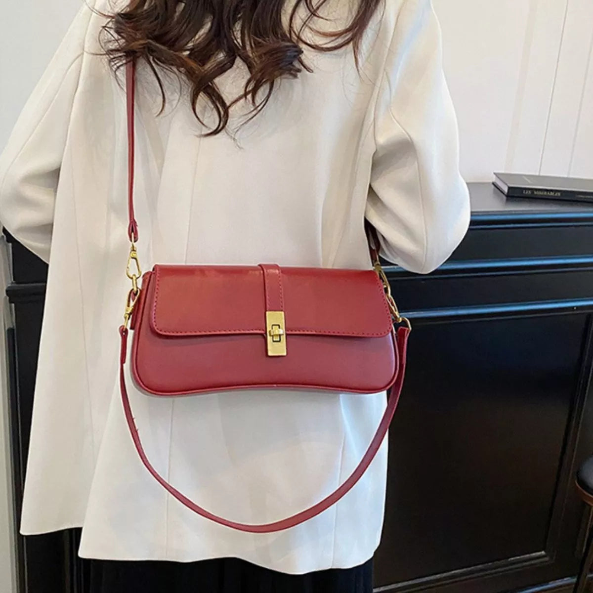 Red rectangular crossbody handbag with a gold turn-lock buckle and adjustable shoulder strap displayed on a modern tabletop.
