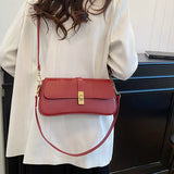 Red rectangular crossbody handbag with a gold turn-lock buckle and adjustable shoulder strap displayed on a modern tabletop.