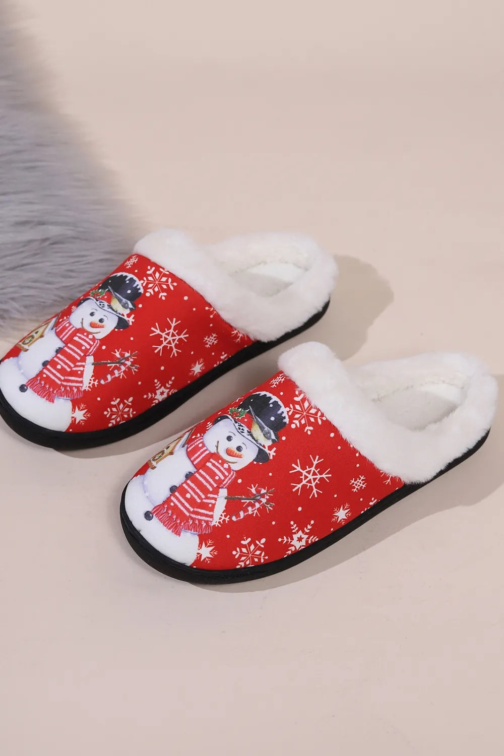Red Christmas snowman slippers with fluffy white faux fur trim, snowflake pattern, round toe, and black flat soles, shown on feet.