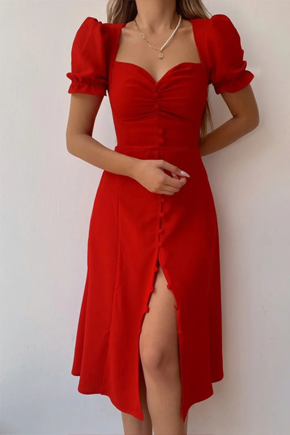 Woman wearing a red sweetheart-neck midi dress with puff sleeves, ruched detailing, and a button-front slit.