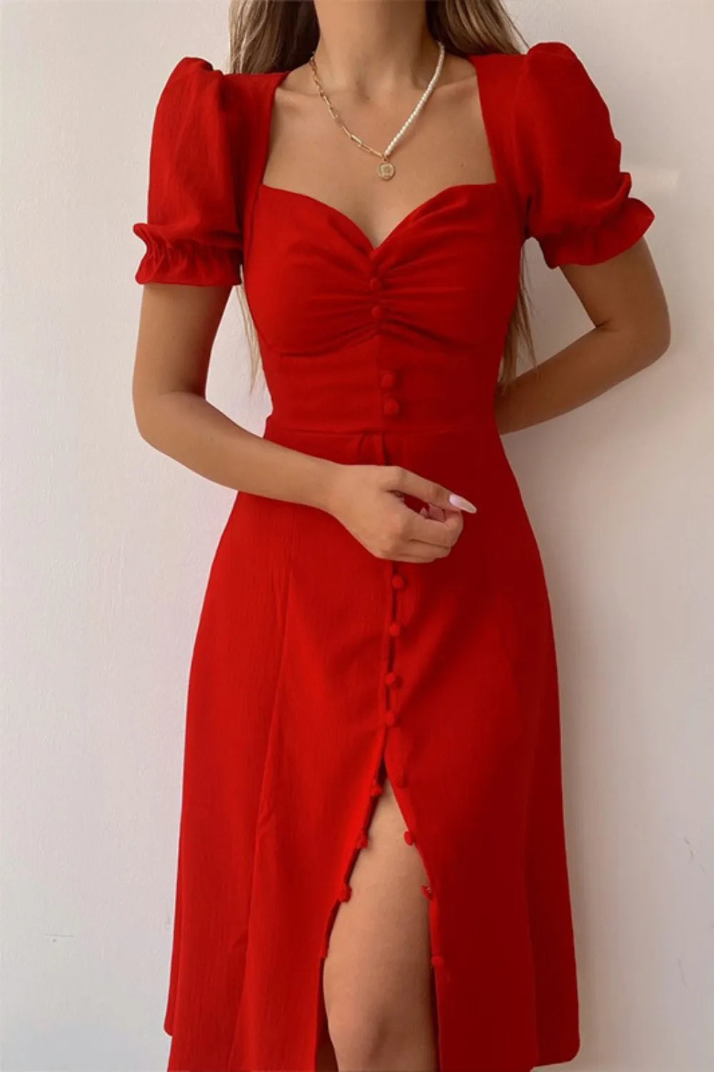 Woman wearing a red sweetheart-neck midi dress with puff sleeves, ruched detailing, and a button-front slit.