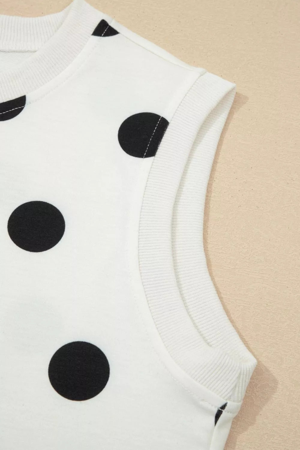 White sleeveless top with black polka dots on a beige background