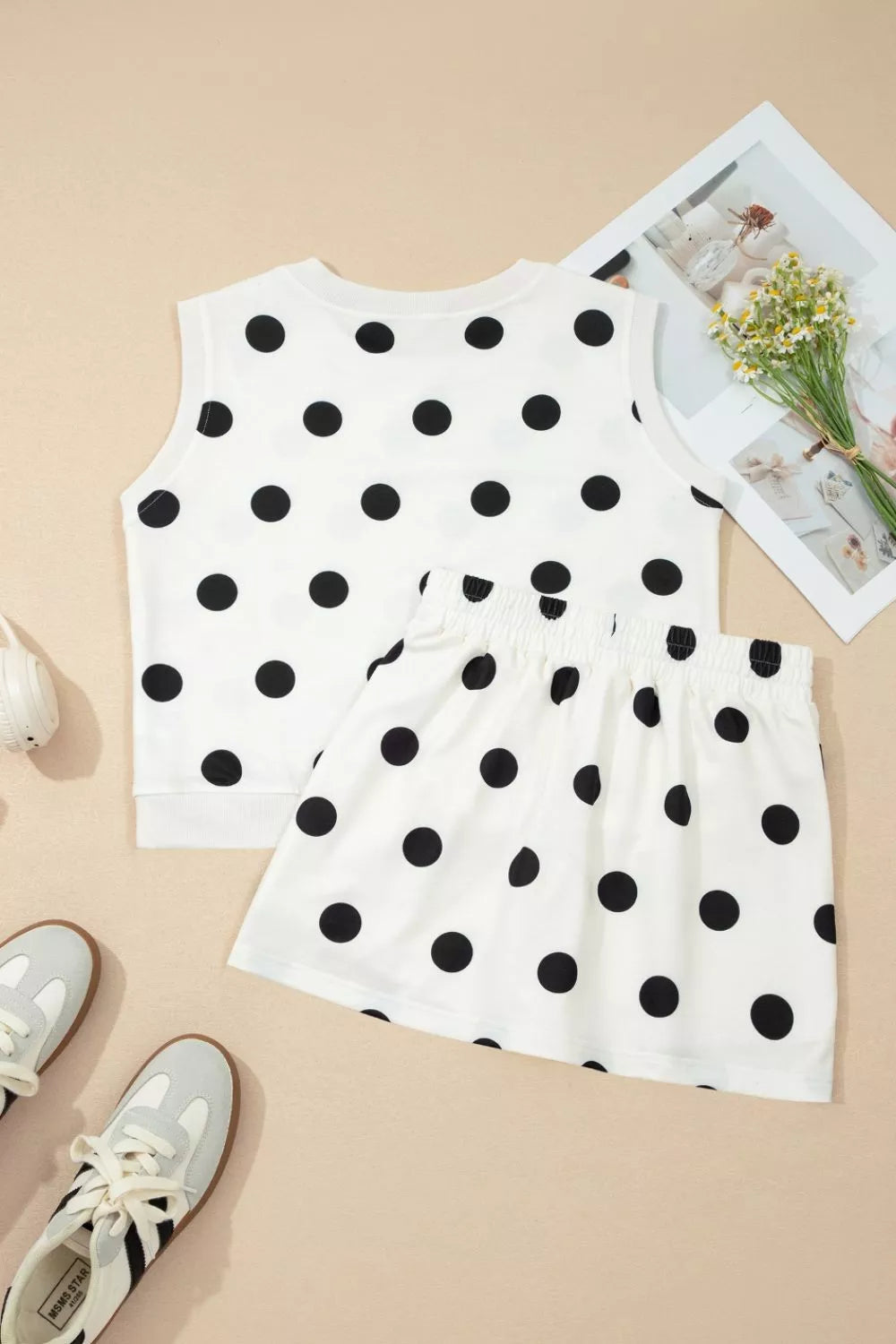 White sleeveless top with black polka dots and matching shorts on a beige background.