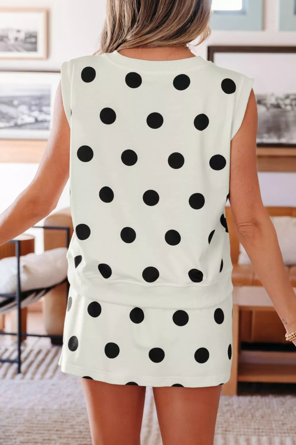 Person wearing a white sleeveless top with black polka dots in an indoor setting.