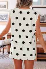 Person wearing a white sleeveless top with black polka dots in an indoor setting.