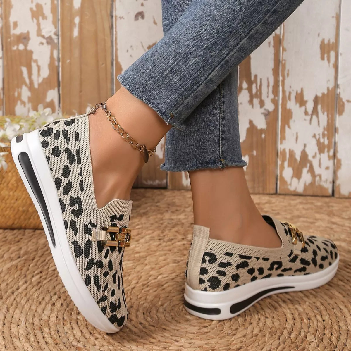 Leopard print slip-on shoes worn with blue jeans on a textured floor.