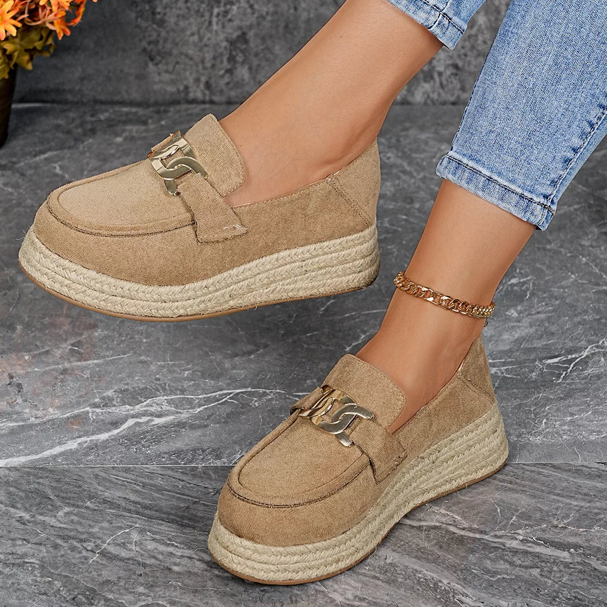 Beige espadrille loafers worn with blue jeans on a gray surface.
