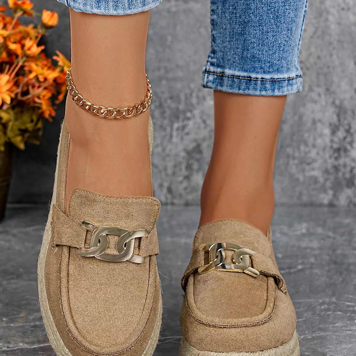 Beige loafers with gold buckles worn by a person, with a blurred background.