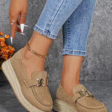 Beige loafers with gold buckles worn with blue jeans against a gray background