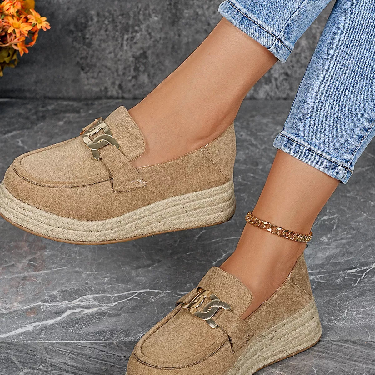 Beige espadrille loafers worn on a gray surface with a blurred background