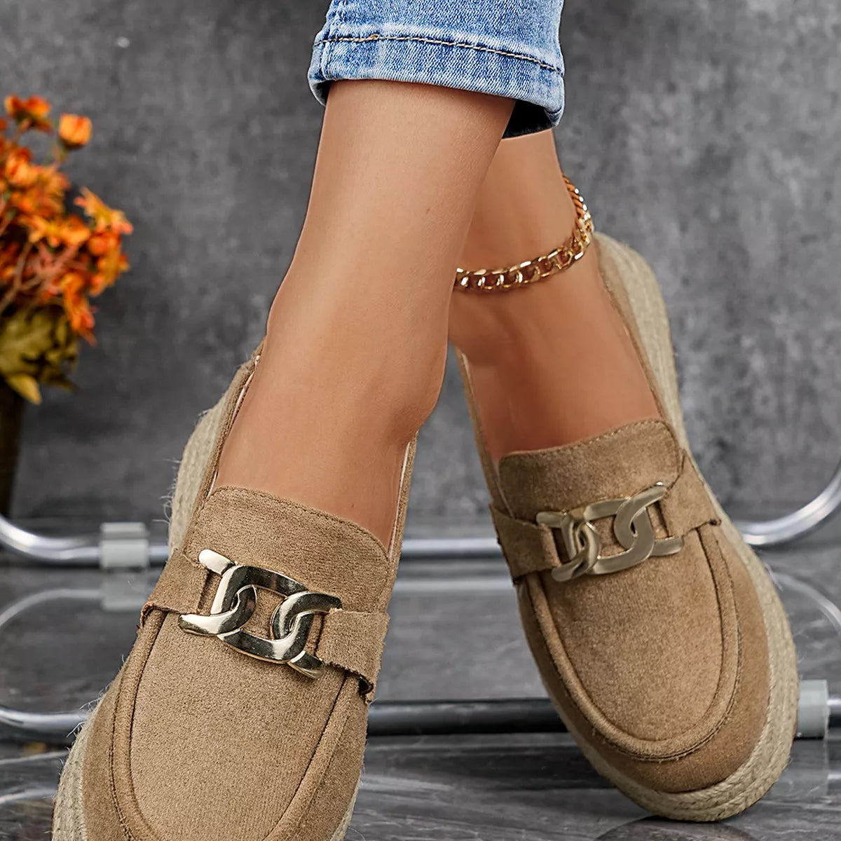 Tan loafers with gold chain details worn by a person, with a blurred background.
