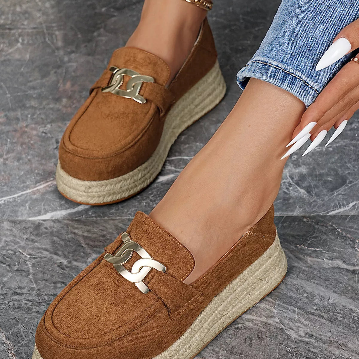Brown loafers with gold buckles worn by a person on a gray marble surface