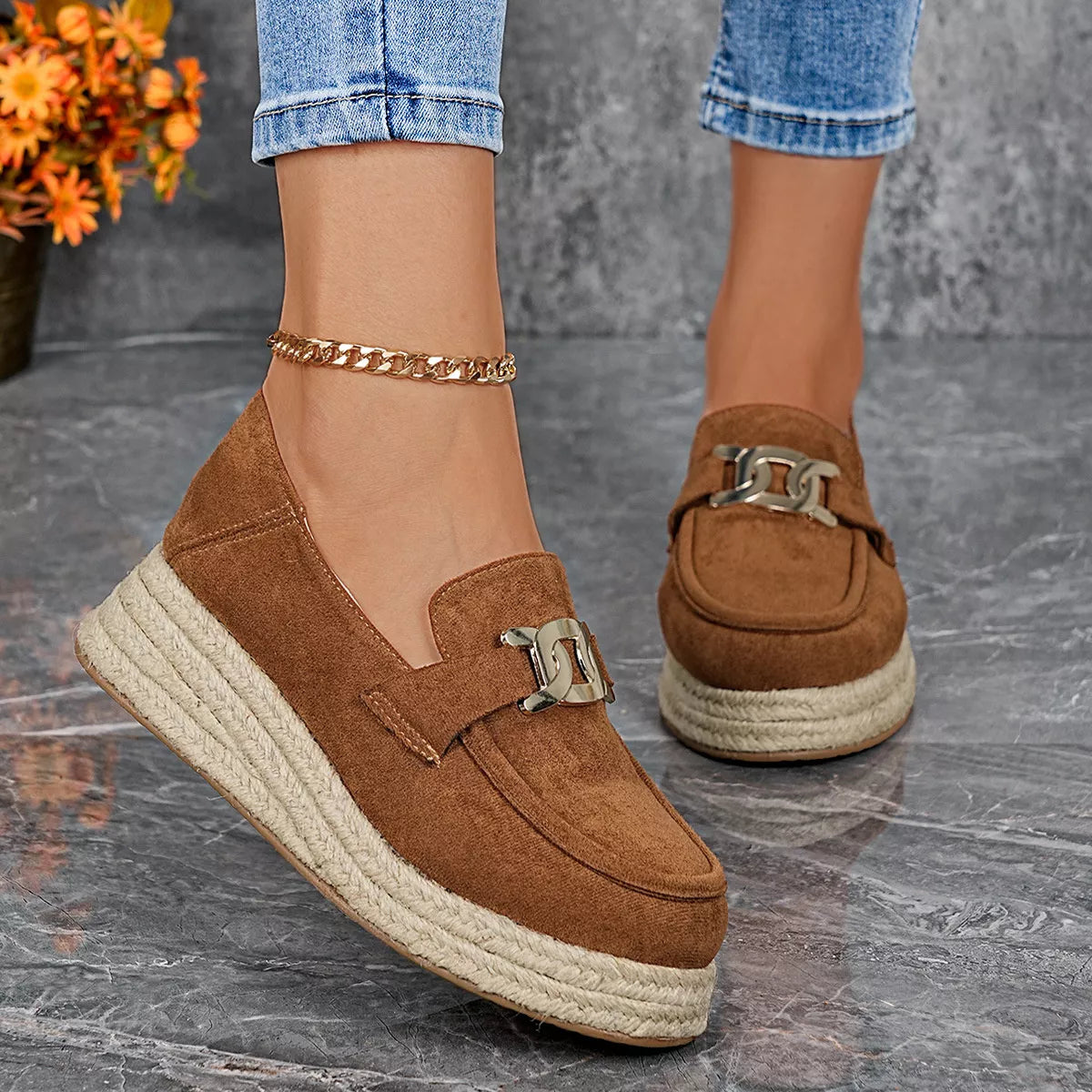 Brown suede loafers with espadrille sole worn by a person on a gray surface.