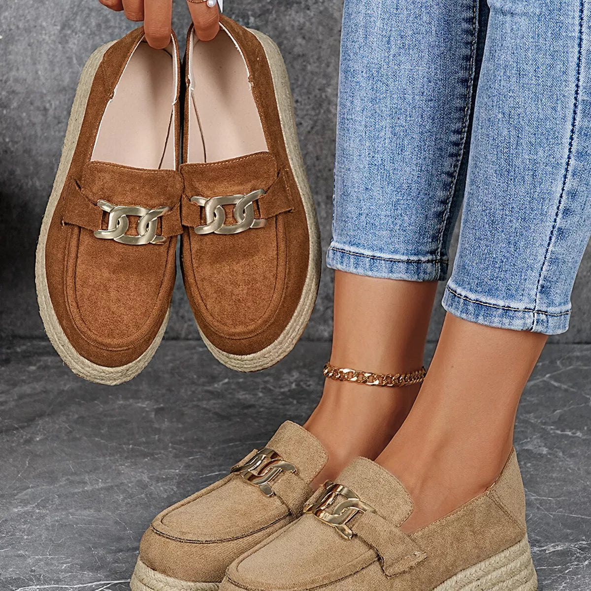Brown loafers with gold accents held by a person wearing blue jeans.