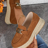 Brown suede espadrille loafers with chain detail held by a hand on a gray surface.