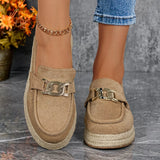 Beige loafers with metal chain details worn by a person on a gray surface.