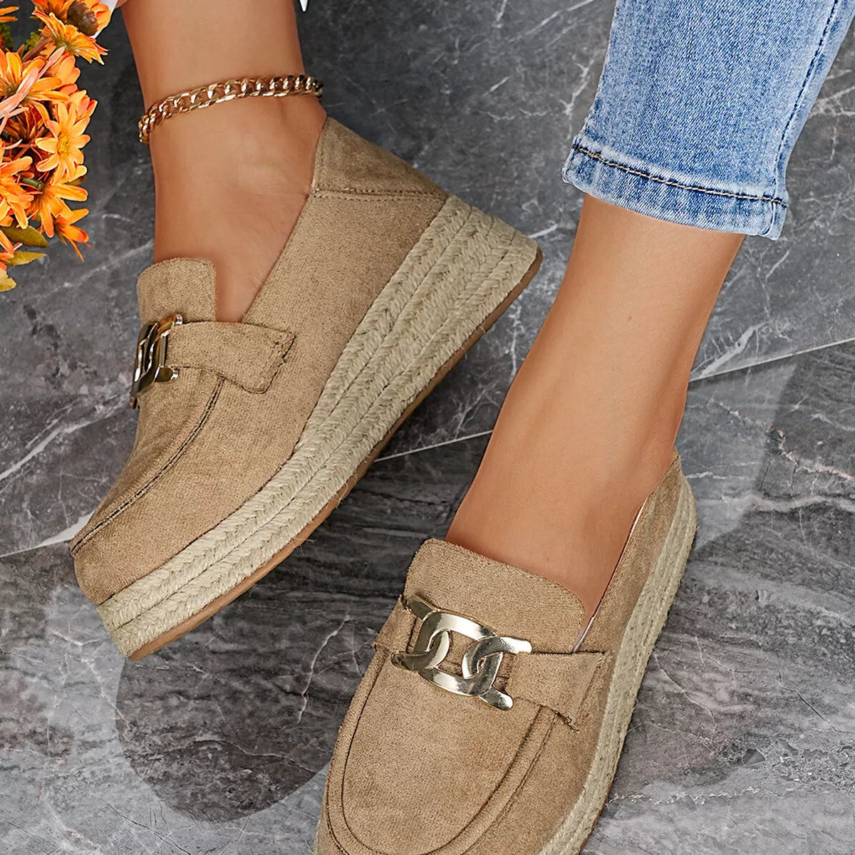 Beige espadrille loafers with chain detail on a stone floor.